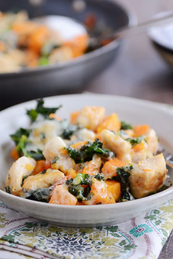 A bowl filled with cubed sweet potato, kale, cooked chicken, and melted cheese.