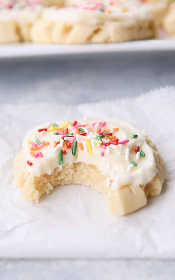 Swig sugar cookie frosted with sprinkles with bite taken out on white napkin.