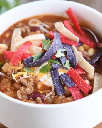 White bowl filled with taco soup, cheese, sour cream and tortilla strips.