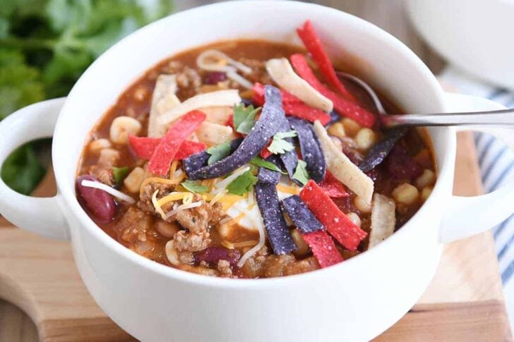White bowl filled with taco soup, cheese, sour cream and tortilla strips.