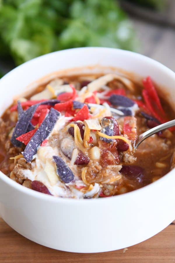 Spoon digging in to White bowl filled with taco soup, cheese, sour cream and tortilla strips.