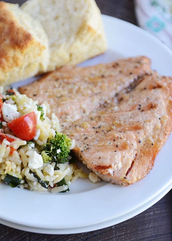 A grilled salmon fillet, biscuit, and helping of pasta salad on a white plate.
