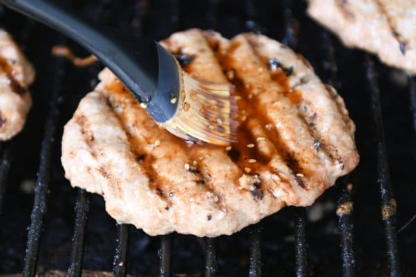 Brushing grilled turkey burger with teriyaki sauce.