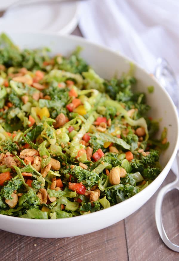 A large white bowl of Thai salad with chopped vegetables, cashews, and chopped kale.