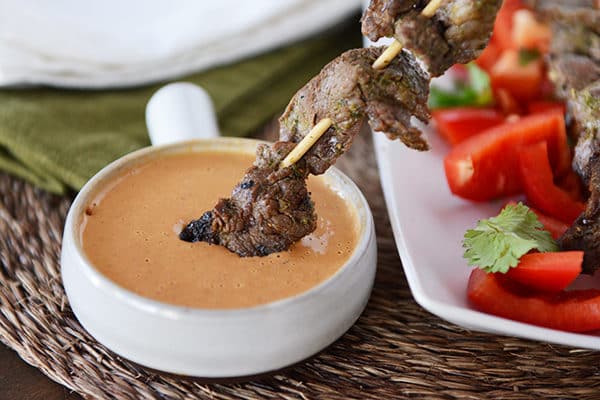 A grilled beef skewer getting dipped in a ramekin of sauce.
