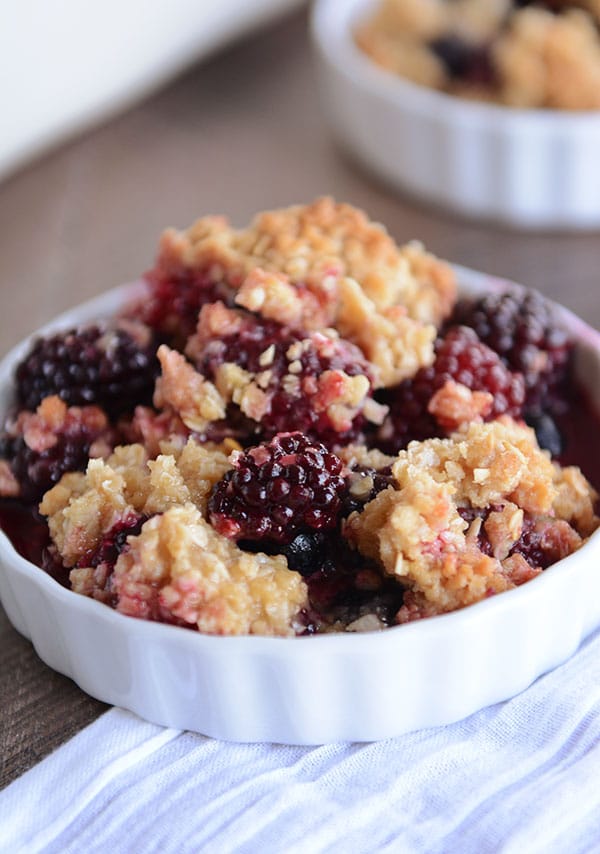 A white dish heaped full of blackberry-studded fruit crisp.