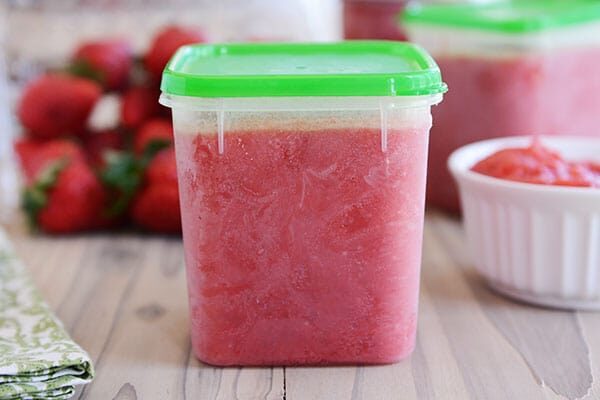 A plastic tupperware of freezer strawberry jam. 