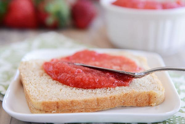 A slice of whole wheat bread getting strawberry jam spread on top.
