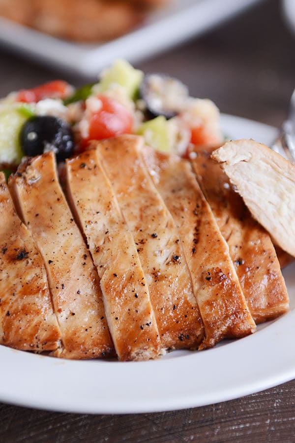 A grilled chicken breast cut in slices next to a quinoa, olive, and tomato salad.