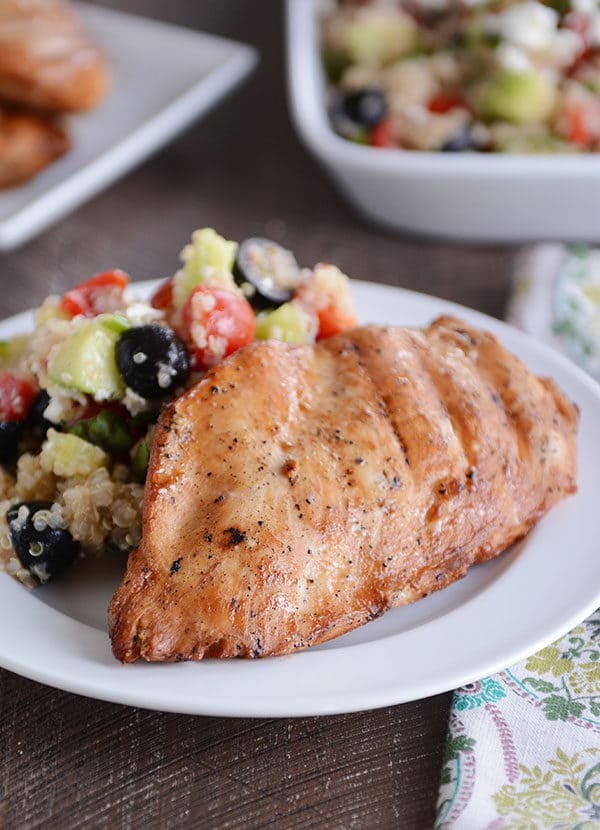 A grilled chicken breast and quinoa vegetable salad on a white plate.