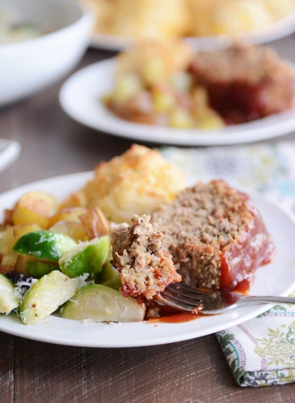 A slice of the best glazed meatloaf on a plate with vegetables and a biscuit.