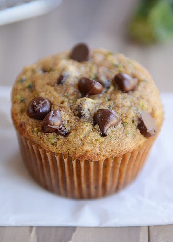 Top view of a chocolate chip topped zucchini muffin on a piece of parchment paper.