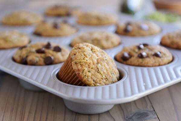 Cooked zucchini muffins in a muffin tin, some topped with chocolate chips and some not.