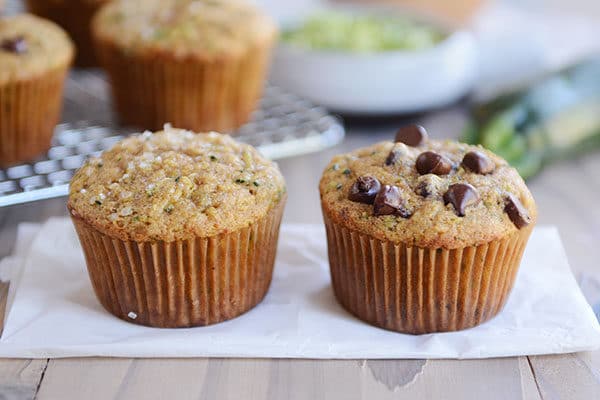 Two zucchini muffins next to each other on a piece of parchment, one with chocolate chips and one without.