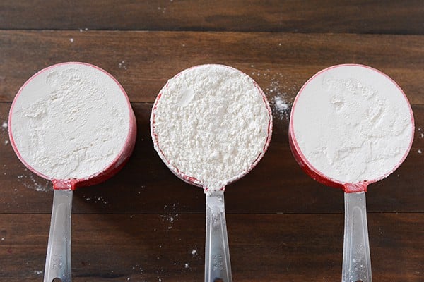 Top view of three measuring cups full of white flour. 