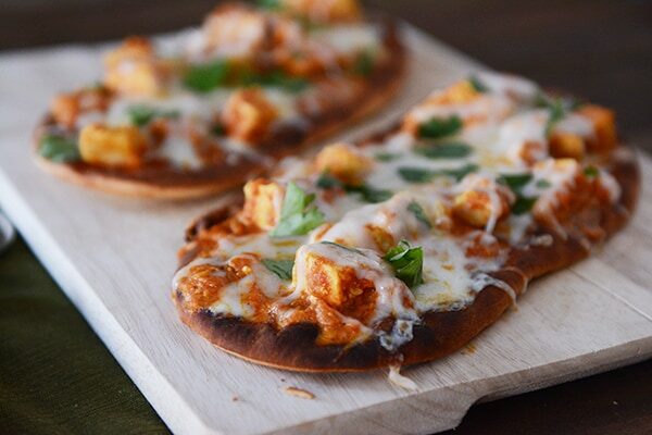 Two cooked cheesy chicken tikka pizzas on a cutting board.