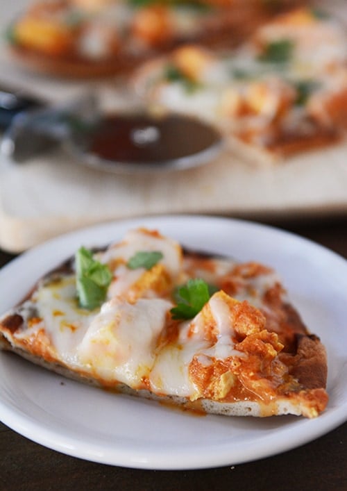 A slice of chicken tikka pizza on a white plate. 