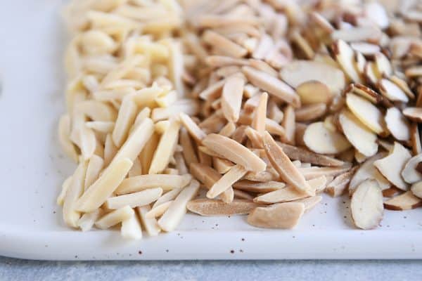 A white plate of toasted and untoasted almonds. 