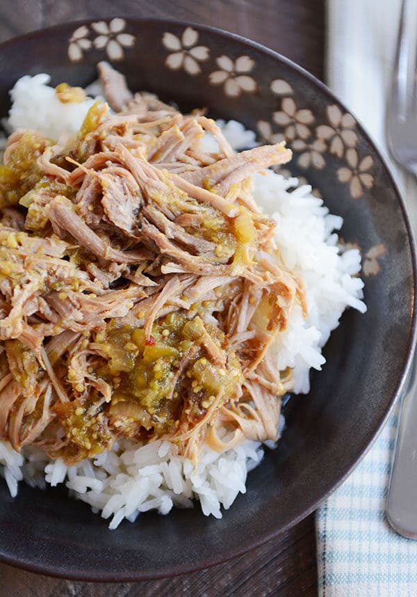 A dark floral bowl of white rice topped with shredded pork and tomatillo sauce. 