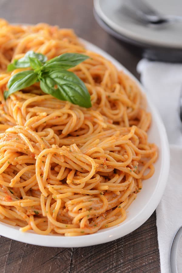 A large oval white bowl full of cooked tomato pesto pasta. 