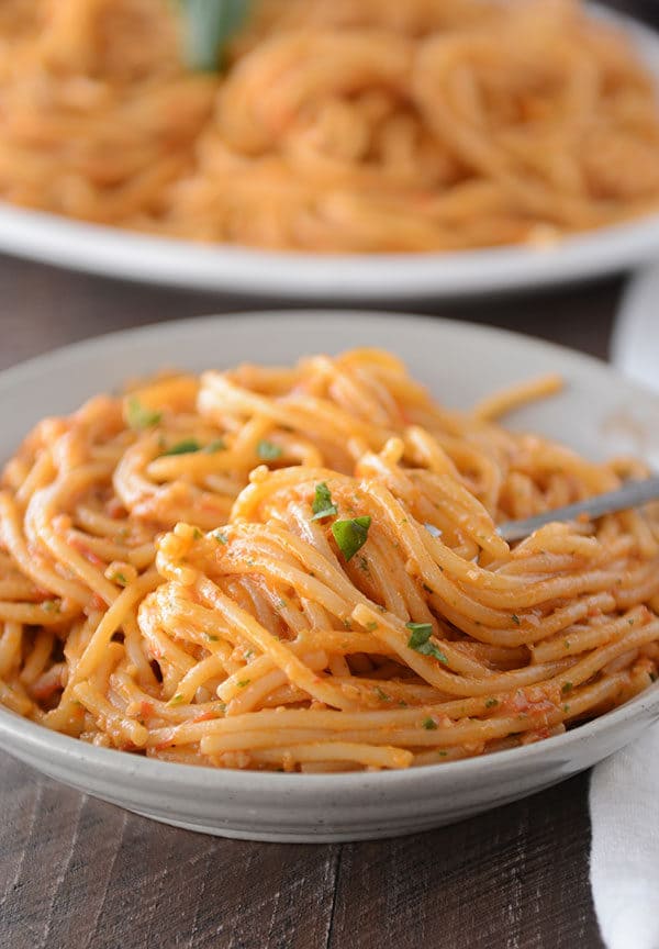 A white bowl of tomato and pesto coated spaghetti noodles.