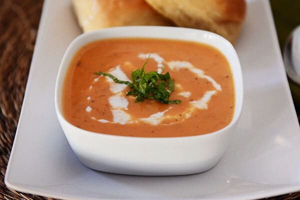 A white bowl of tomato soup with a swirl of whipped cream in it. 