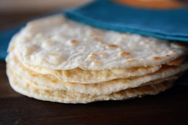 A stack of homemade cooked tortillas under a blue napkin. 