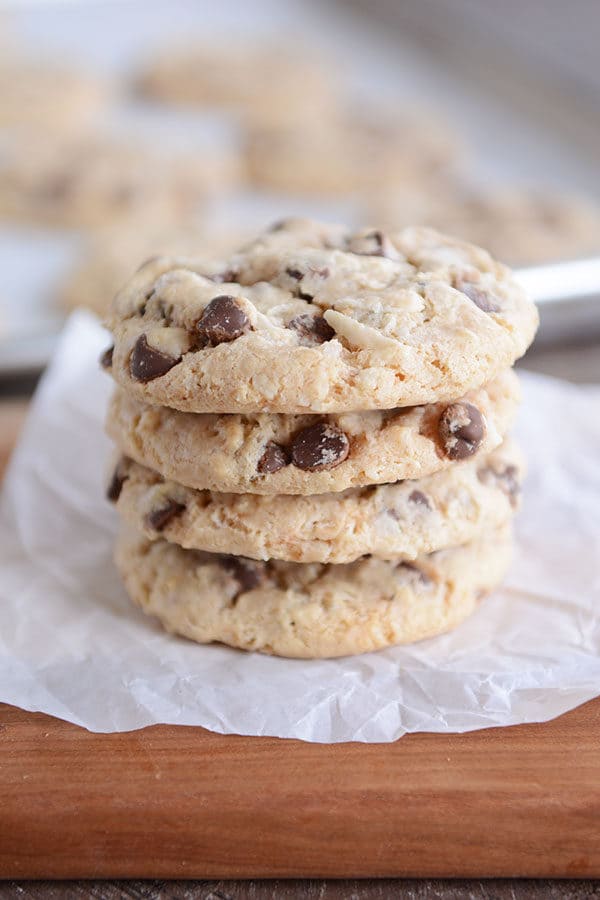 Four chocolate chip cookies stacked on top of each other on a piece of parchment paper.