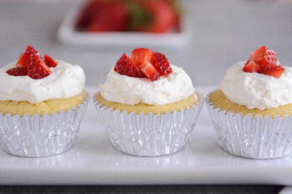 Three tres leches cupcakes in silver muffin liners lined up on a white platter.