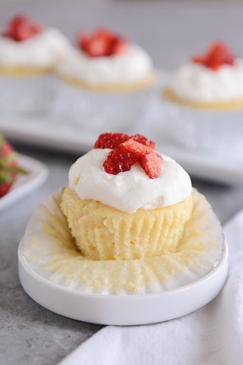 A tres leches cupcakes topped with frosting and chopped strawberries on a white muffin liner.