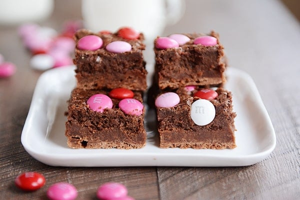 Four M&M topped truffle brownies on a white square plate.