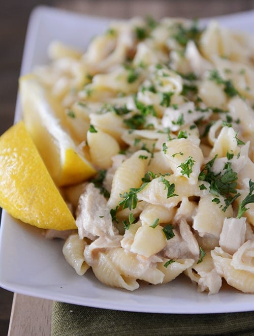 A white platter with creamy tuna and pasta shells with lemon slices on the side.