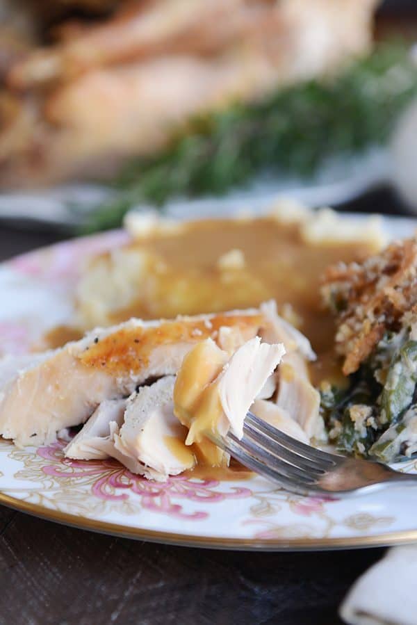 A fork taking a bite of turkey covered with gravy off of a plate.