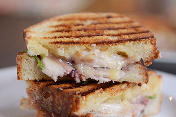 A turkey brie panini cut in half and stacked on a white plate.