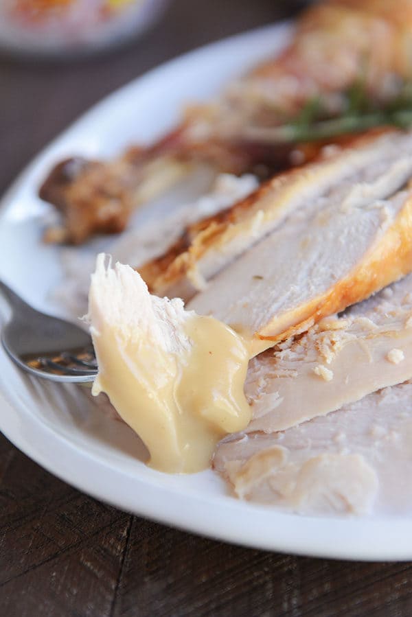 A fork taking a bite of turkey off of a platter of turkey slices.