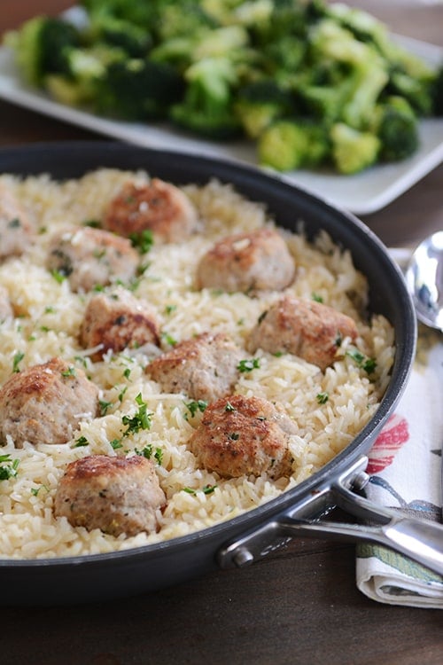 A skillet full of rice and meatballs, with a plate of roasted broccoli in the background.