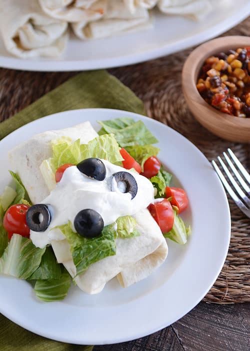 A burrito topped with lettuce, olives, sour cream and tomatoes. 