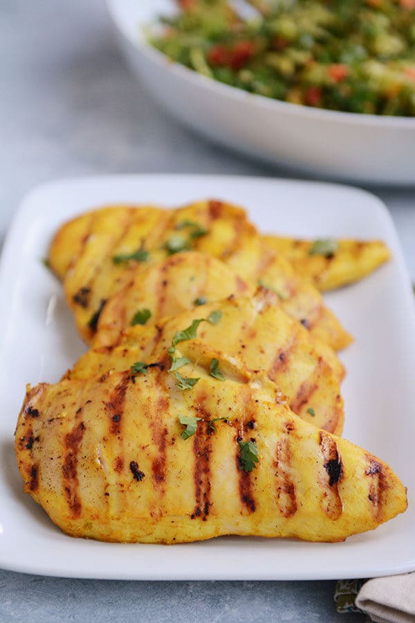A white platter filled with grilled chicken, sprinkled with cilantro. 