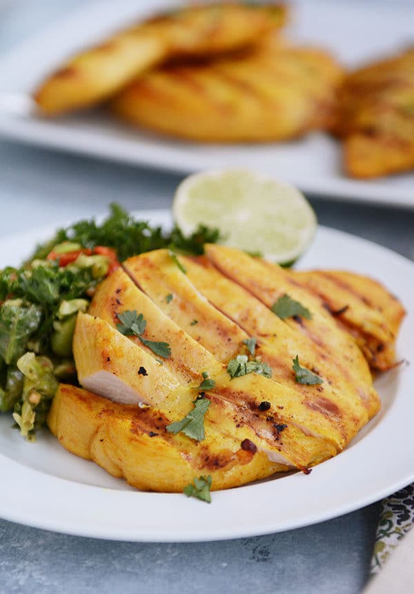 A white plate with sliced grilled chicken and a green salad and slice of lime on the plate.