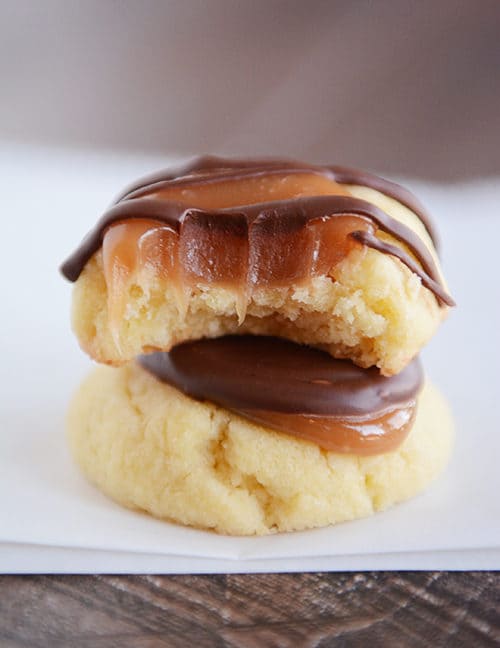 Two caramel, chocolate shortbread cookies stacked on each other, with the top one with a bite taken out.