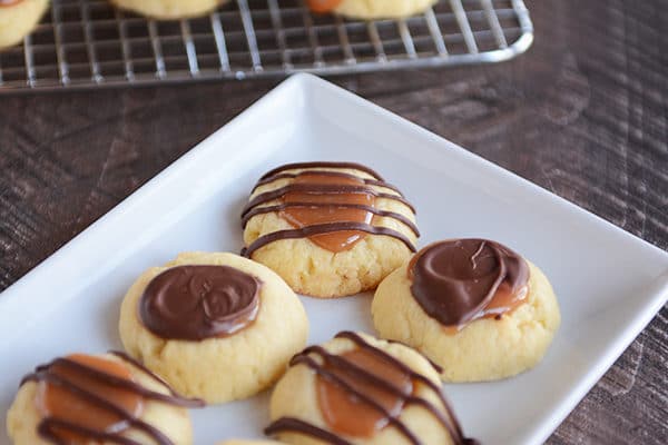 Chocolate and caramel topped shortbread cookies on a white rectangular platter.