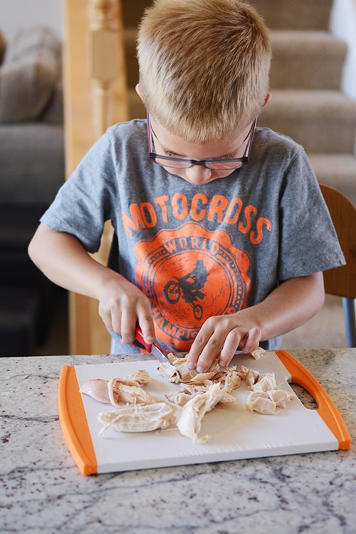 A little boy cutting up chicken on a cutting board. 
