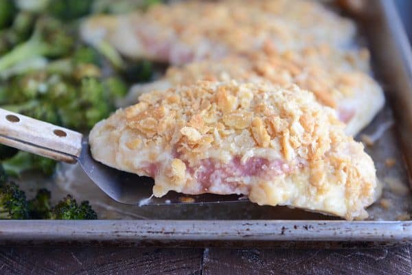 Lifting unstuffed sheet pan chicken cordon bleu with spatula.