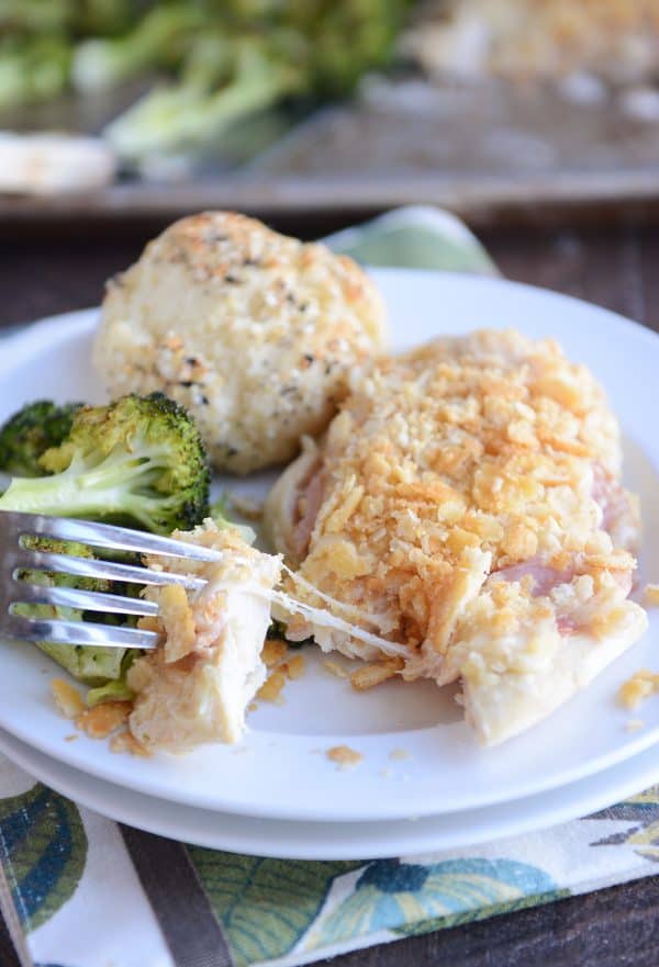 Taking a bite out of unstuffed sheet pan chicken cordon bleu on white plate.