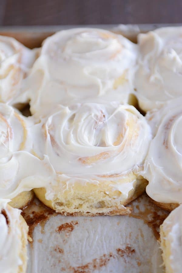 A pan of frosted cinnamon rolls with one taken out. 