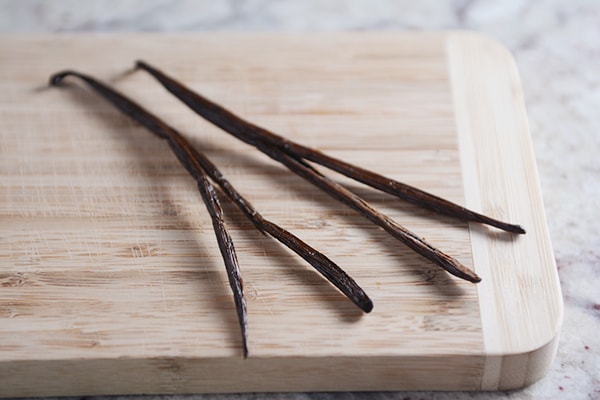 Four vanilla beans laying on a cutting board. 