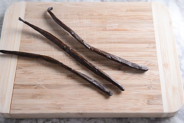Three vanilla beans laying on a cutting board. 