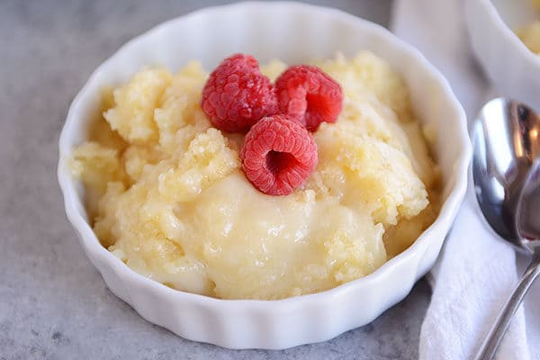 A small white ramekin full of vanilla pudding cake topped with three fresh raspberries.