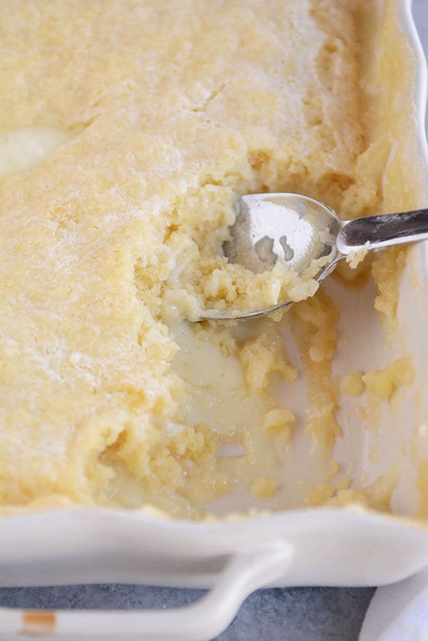 Top view of a white dish full of vanilla pudding cake with a spoon in the side and a scoop taken out.