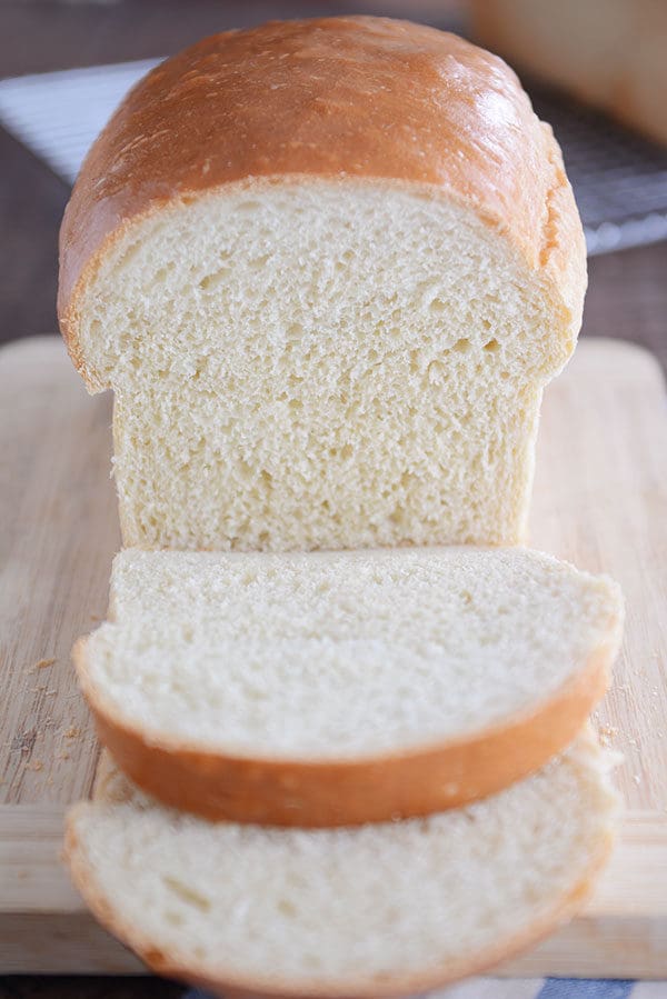 A loaf of white sandwich bread, with two slices cut off the front and laying in front.